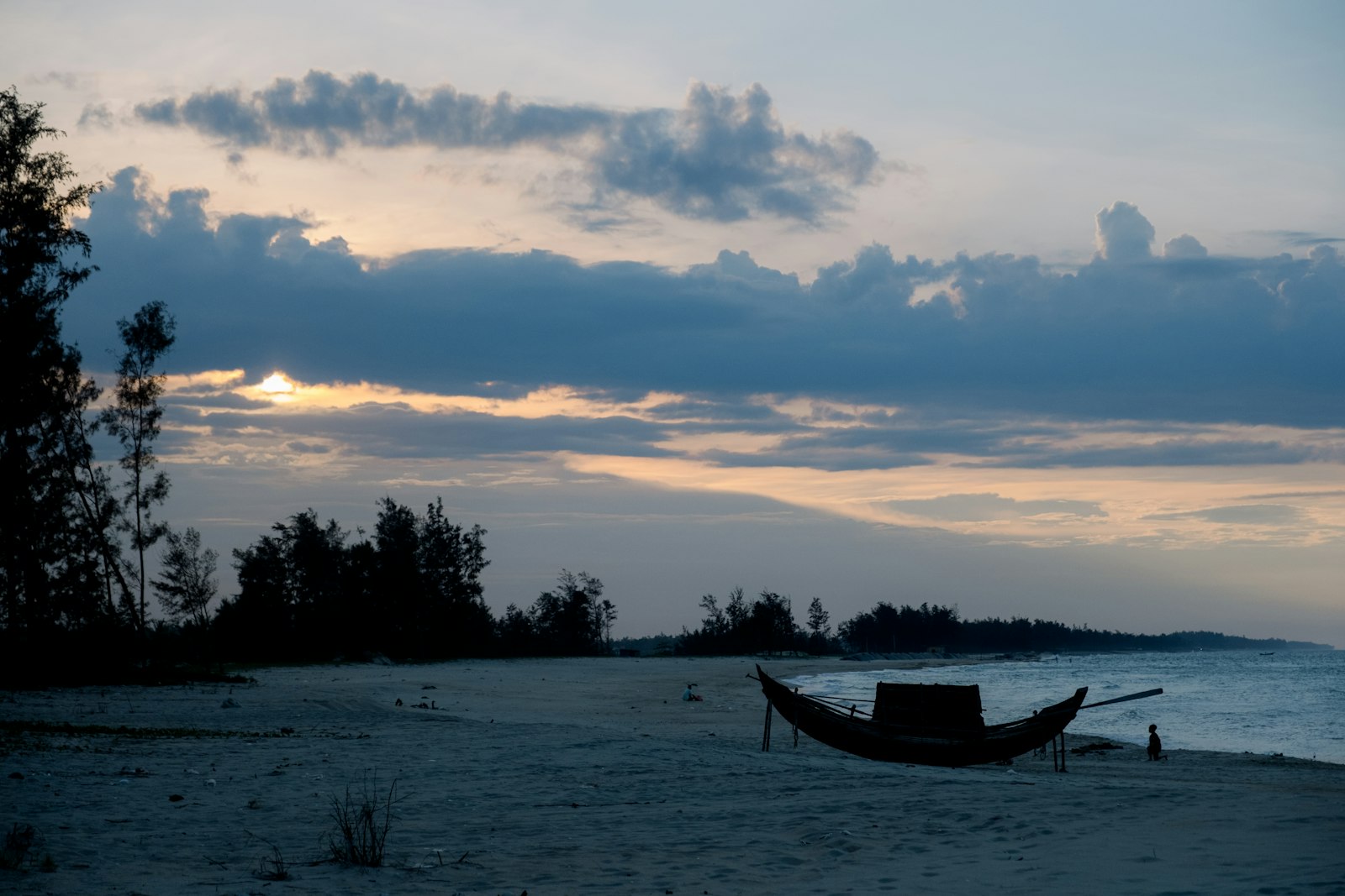A boat rests on the sandy shore at dusk.